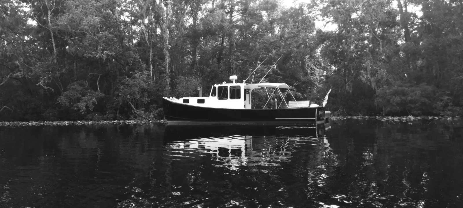 A boat moored on a tree-lined river, in black and white