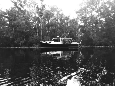 A boat moored on a tree-lined river, in black and white