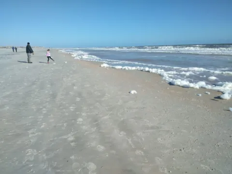 A long beach with a dog walker far down the shore