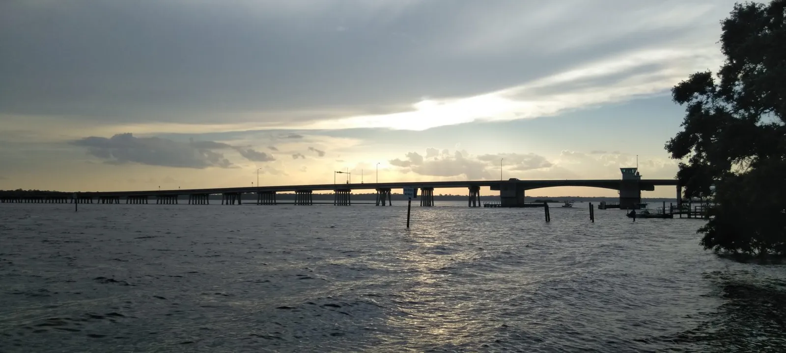 A long bridge over dark water under a cloudy sky