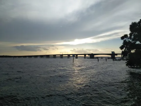 A long bridge over dark water under a cloudy sky