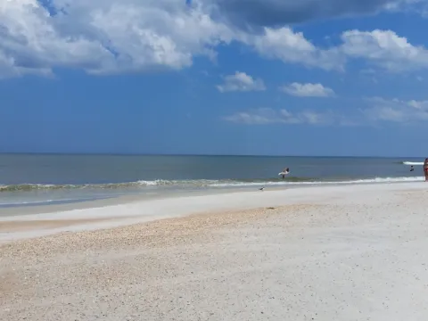 Beach sand and gentle surf beneath towering white clouds.