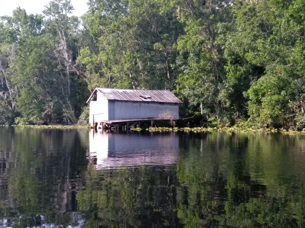 A small boathouse on a quiet, tree-lined river.