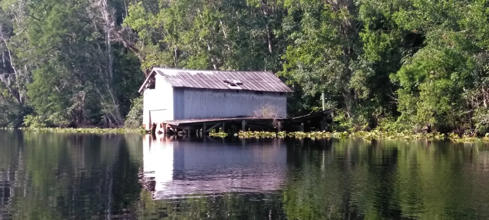 A small boathouse on a quiet, tree-lined river.