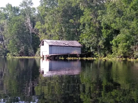 A small boathouse on a quiet, tree-lined river.