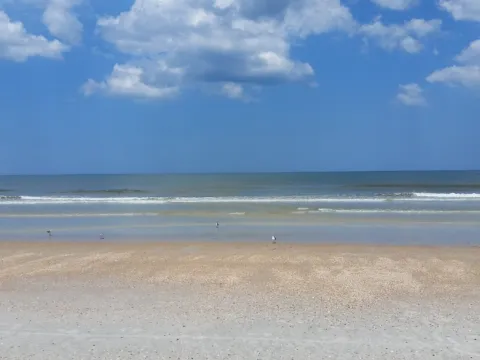 A broad sandy beach with low surf under big white clouds.