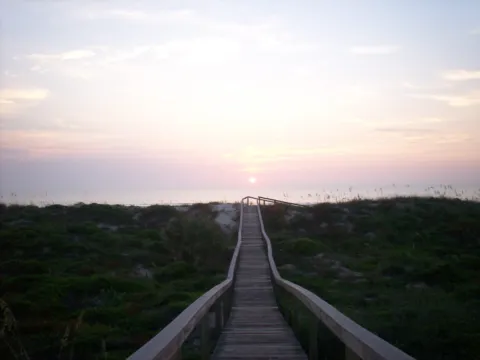 A wooden boardwalk crossing the dunes to the beach at sunrise.