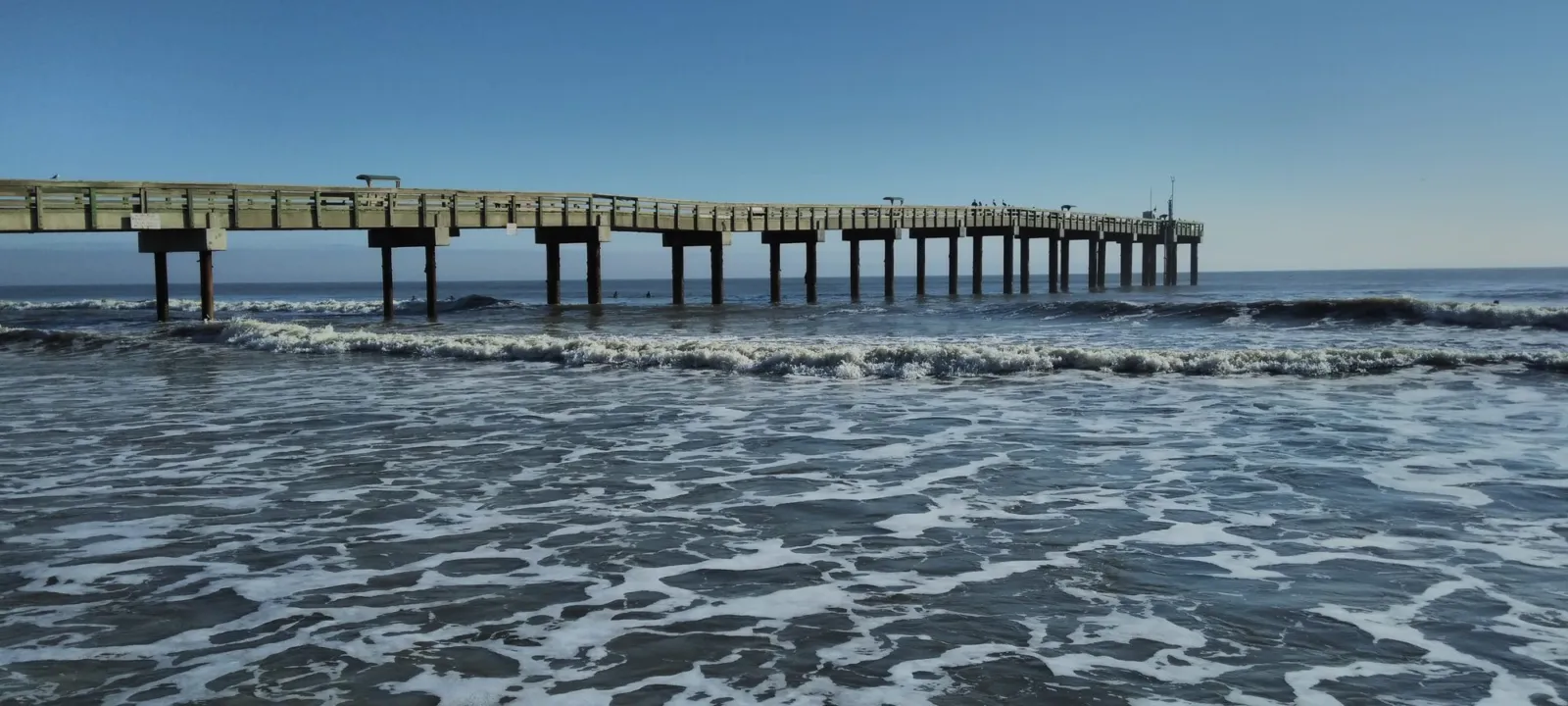 A long fishing pier reaching out over blue water on a clear day.