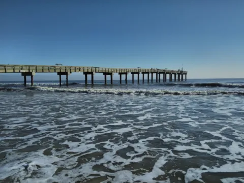 A long fishing pier reaching out over blue water on a clear day.