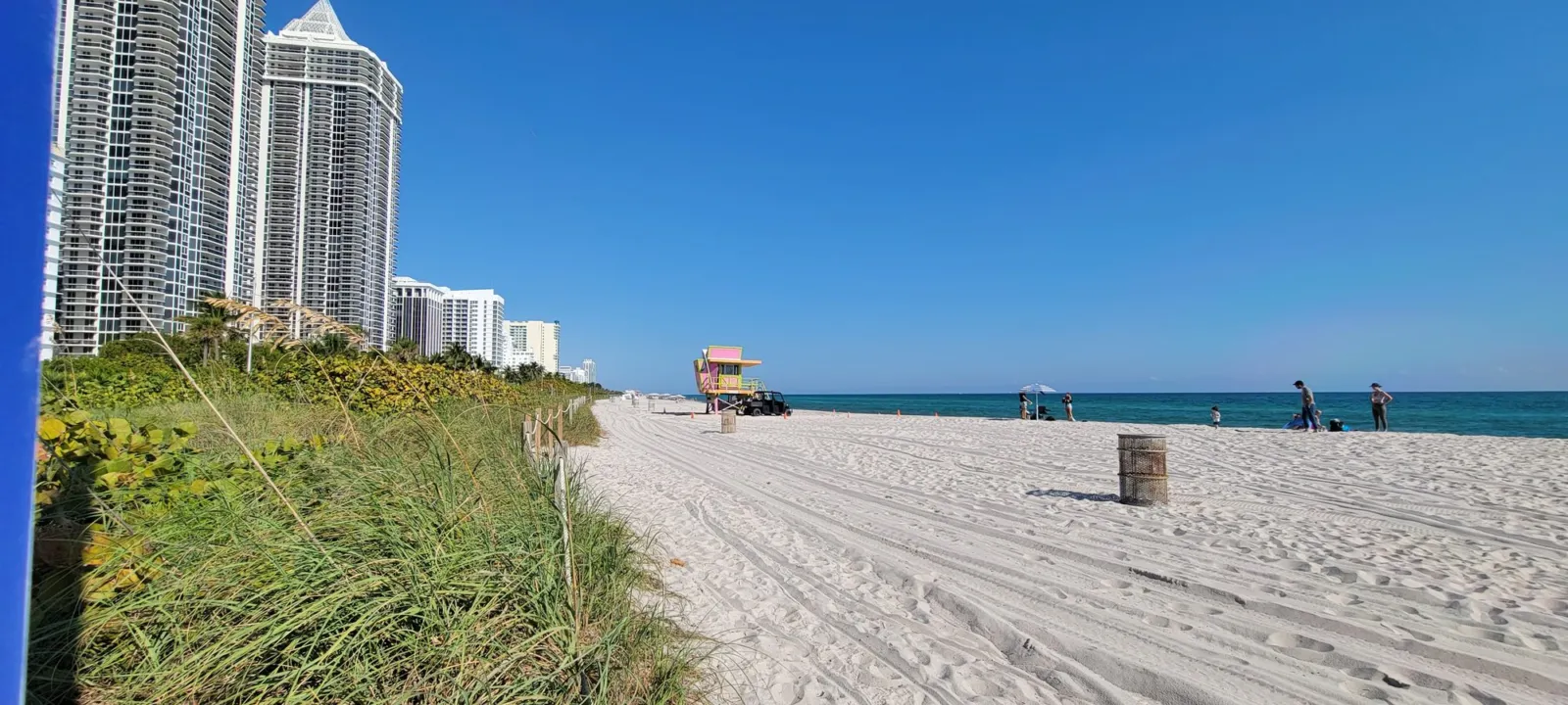 A wide stretch of pale sand at Miami Beach with turquoise water and a lifeguard stand in the distance.