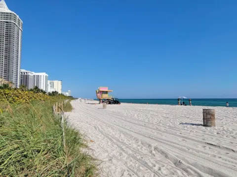A wide stretch of pale sand at Miami Beach with turquoise water and a lifeguard stand in the distance.