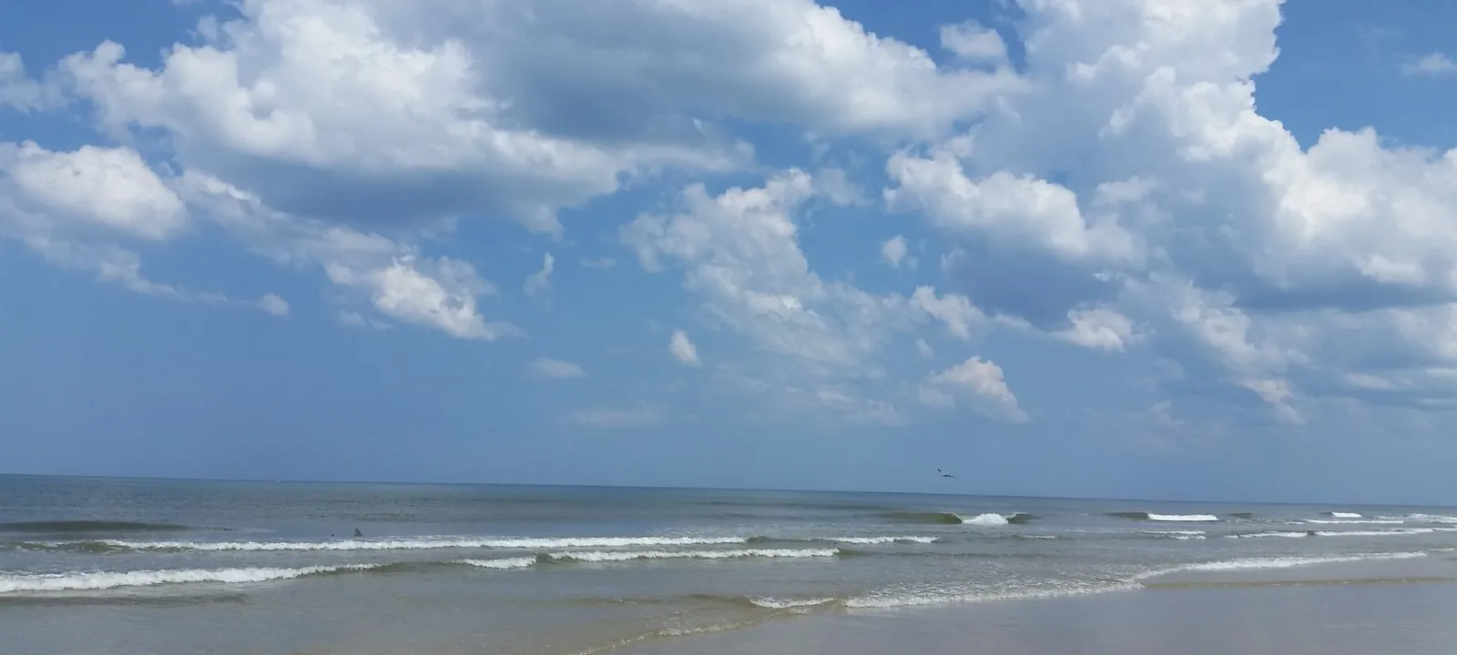 A beach at midday with scattered clouds over the water.