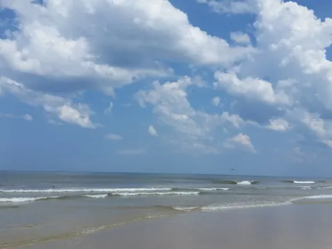 A beach at midday with scattered clouds over the water.