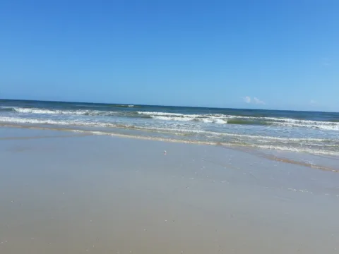An open beach and blue water under a clear sky.