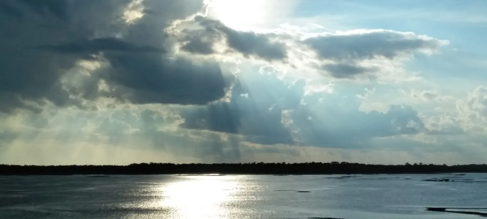 Sun breaking through clouds over bay water