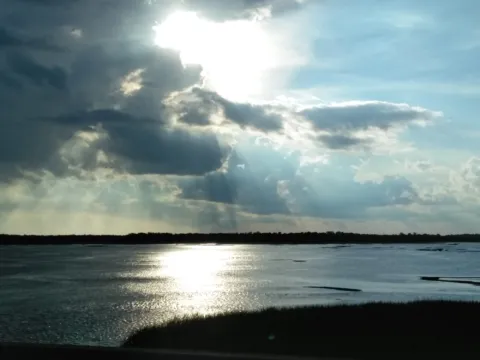 Sun breaking through clouds over bay water