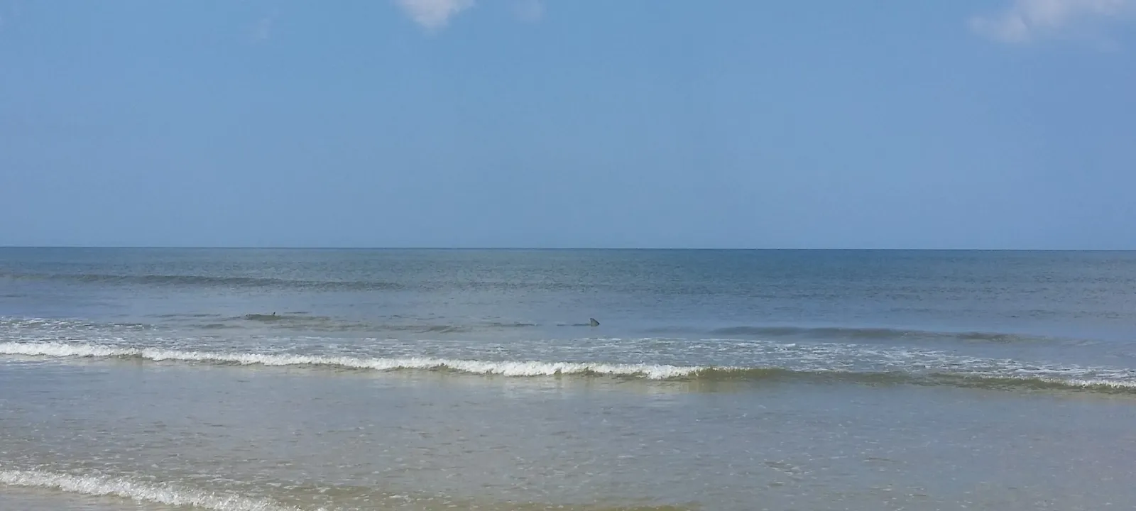 Surf rolling onto a flat, sandy shoreline.