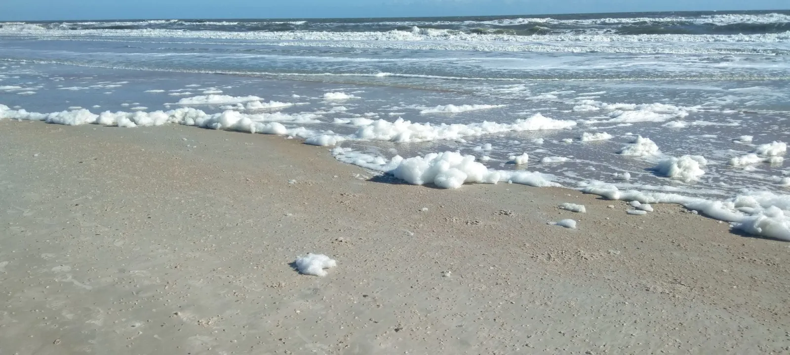 Waves washing onto a sandy beach under a blue sky.