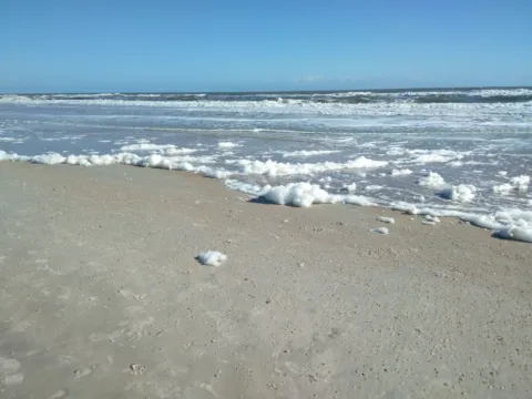 Waves washing onto a sandy beach under a blue sky.