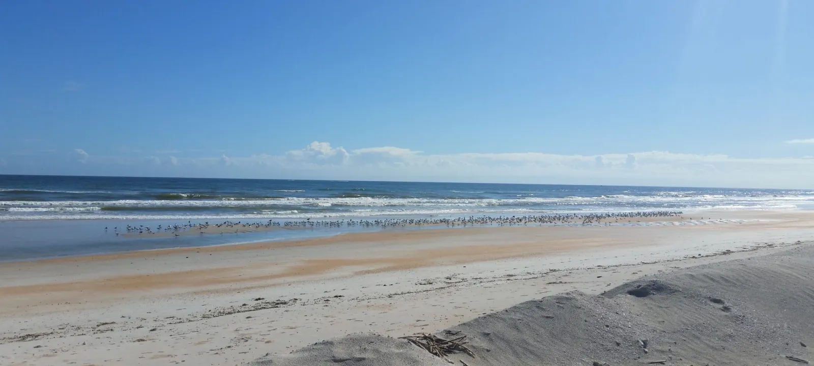 A wide, empty beach under a blue sky with scattered clouds.