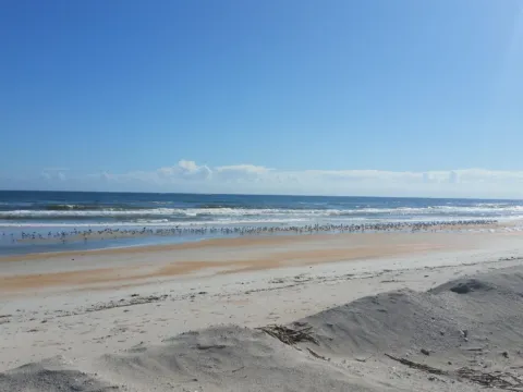 A wide, empty beach under a blue sky with scattered clouds.